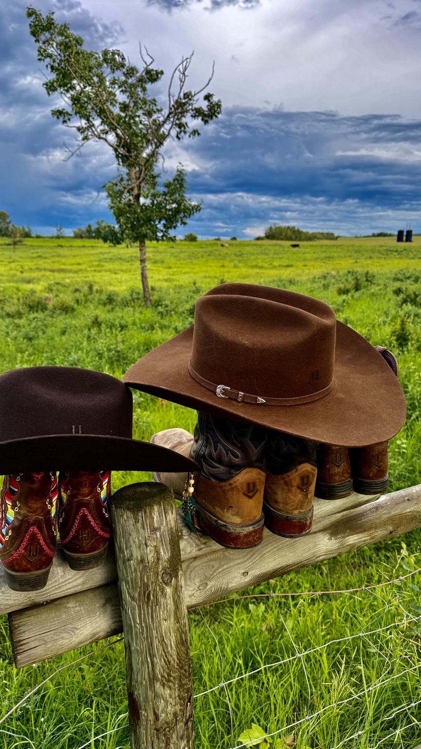 Ranch boots and hats on a fence overlooking green pasture